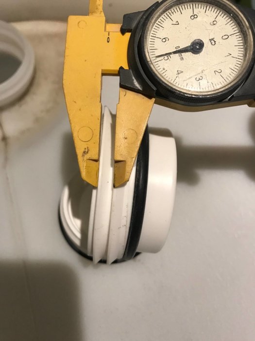 Skjutmått mäter diameter på en vit plastplugg med svart och vit profilering mot en vit bakgrund.
