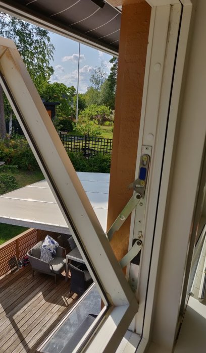 Uppvridet normalöppet fönster med utsikt över trädgård och altan.
