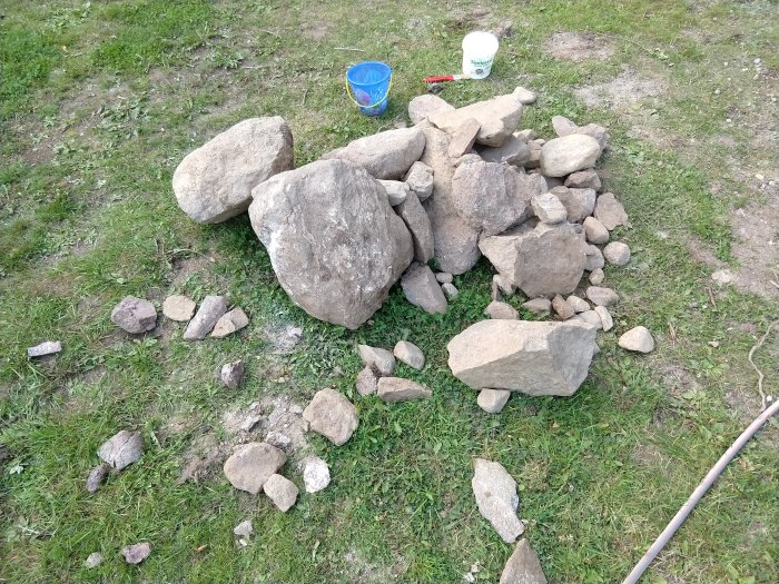 Stor stenhög på gräs med spade och hink i bakgrunden, resultat av grävning.