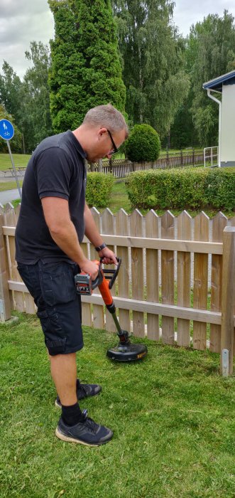 Man använder en tyst batteridriven grästrimmer vid ett staket.