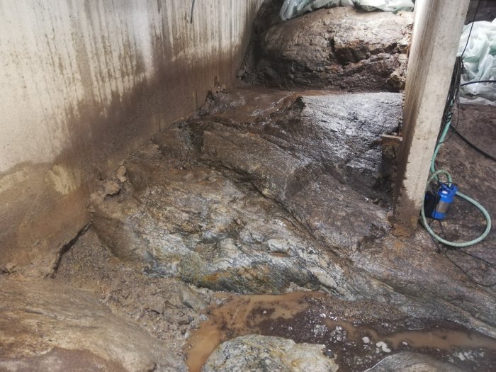 Ongoing basement excavation with exposed rocky substrate, standing water, and construction tools.