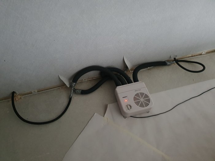 Avfuktare med slangar installerad vid en skadad vägg för att torka ut gips efter vattenskada.