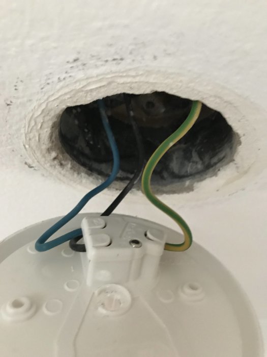 Öppet vägguttag med blå och gul/grön elkabel framför en takspotplatta redo för installation av LED-dimmer.