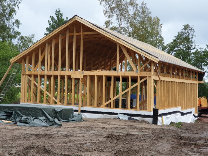 Trästomme av ett garage under konstruktion med en del av taket täckt med råspont och en stege på sidan.