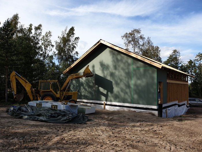 Garage under konstruktion med nyuppsatt utegips och råspont, framför en grävmaskin.