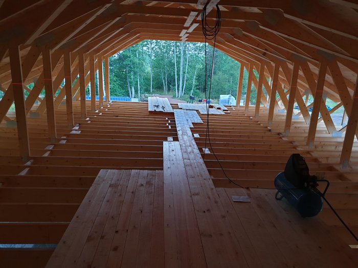 Interiör av ett garage under konstruktion med råspont på golvet och takstolar i trä.