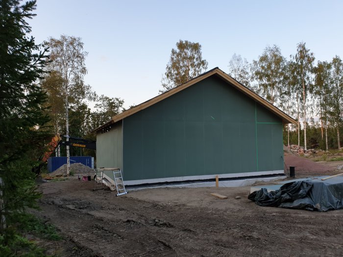 Garage under uppbyggnad med grön väggskiva, väderskyddad med plast och byggtrappa framför.