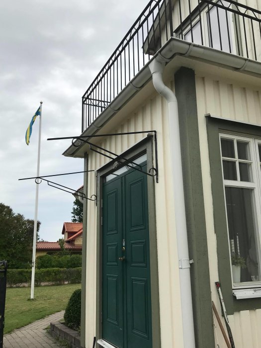 Del av ett hus med en grön dörr, fönster, och en konsoll utan tak som saknar färg och ser sned ut.