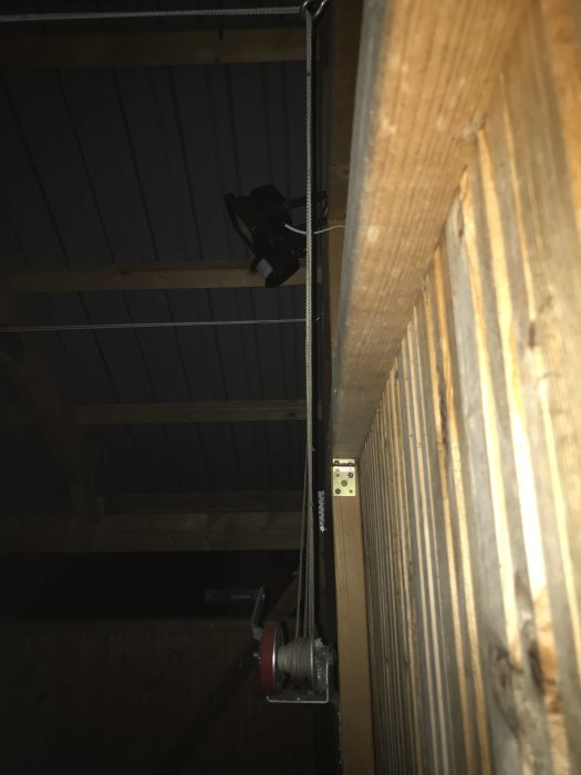 Båtvinsch monterad på vägg med rep genom öglor i taket, i mörkt rum.