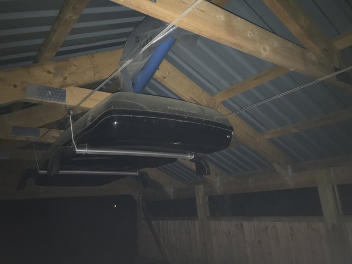 Takmonterad båtvinsch och rep som håller upp en takbox i mörkt förråd.