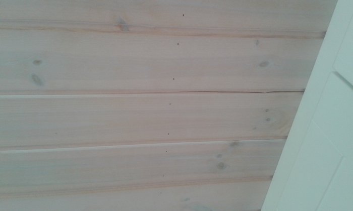 Lång spricka i vitt träkökstak som sträcker sig från skåpets kant mot väggen, med andra mindre sprickor synliga.