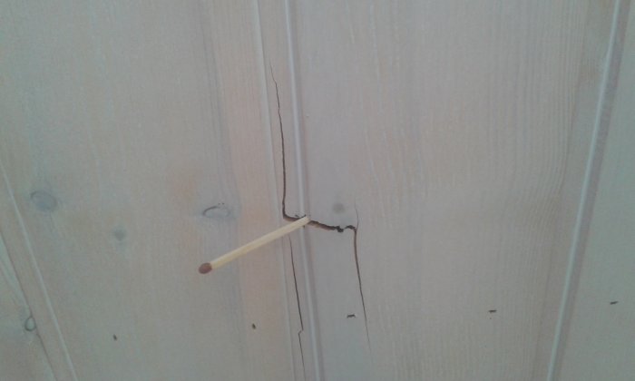 Spricka i en träpanel med en tändsticka som referens för storleken.
