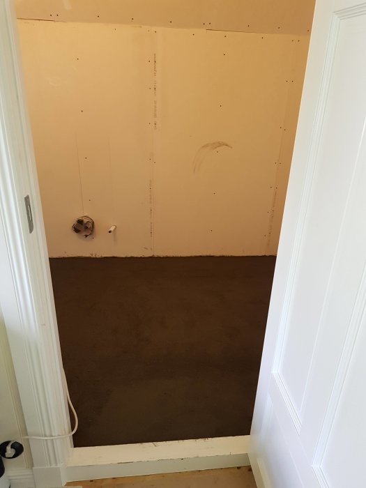 Ett nyligen spacklat golv i ett rum under renovering med väggplattor och rörinstallationer synliga.