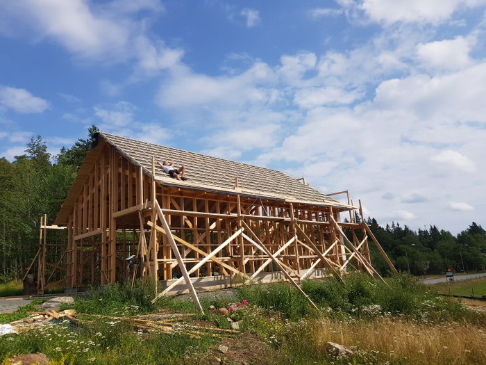 Halvfärdig trästomme till ett hus med öppen takkonstruktion under en klarblå himmel.