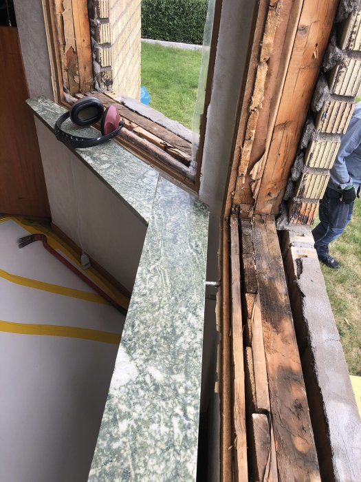 Öppet fönsterutrymme i byggfas med synlig träram och isolering, verktyg på fönsterbrädan, utkik mot trädgård.