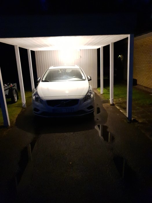 Bil parkerad under renoverad carport med nytt tak och tända lampor på natten.