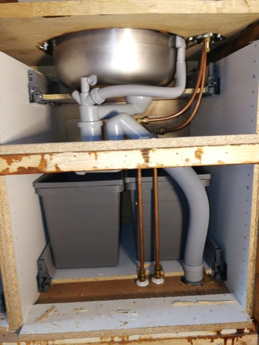 Vattenanslutningen under en bar: kopparledningar, avstängningsventiler och avloppsslangar.