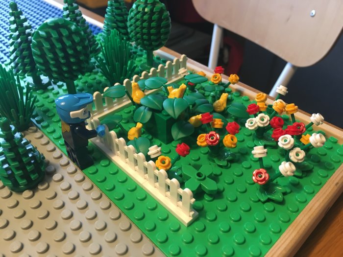 Legofigur i en modellträdgård med gröna växter och färgglada legoblommor, som symboliserar parkslide.