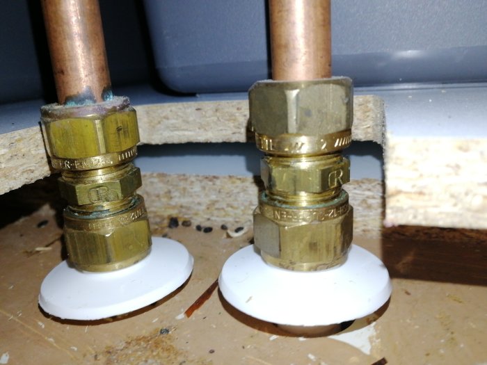 Vattenledningsrör med mässingskopplingar och vita pluggar mot en vägg.