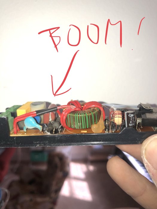 Hand håller en bränd transformator med en markerad skadad komponent och ordet "BOOM!" skrivet överst.