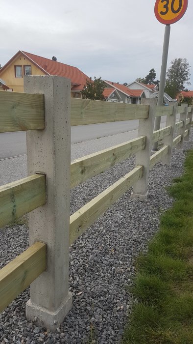 Staket med horisontella träribbor monterade mellan vertikala betongstolpar längs en väg.