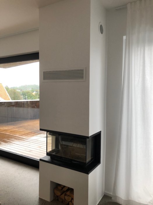 Inbyggd Contura i50 kamin med vedfack och anpassad ventilation över i ett modernt vardagsrum.