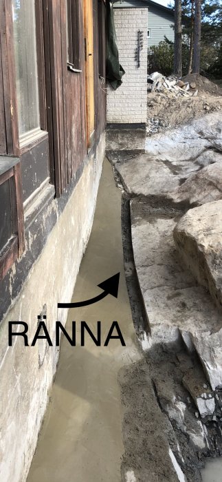 Husgrund med en utgrävd ränna längs väggen och texten "RÄNNA" som visar var arbetet ska utföras.