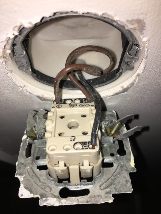 Öppen väggströmbrytare med synliga ledningar och anslutningar, demonterad och med tecken på osäker installation.