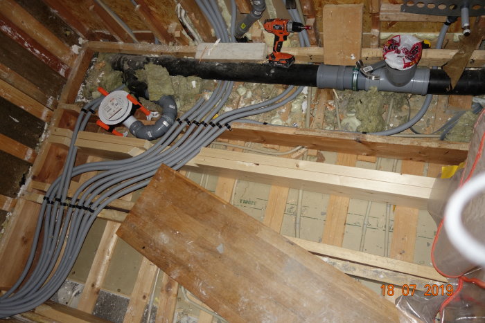 Golvbjälklag med nya reglar och VVS-urtag under renovering av badrum, synlig golvvärme och rörinstallationer.