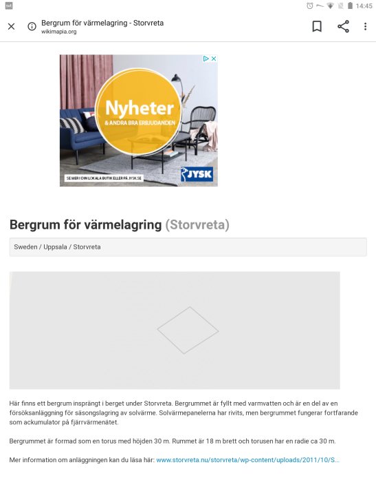 Reklamskylt för Nyheter och erbjudanden från JYSK framför en blå soffa och en vägg med tavlor.