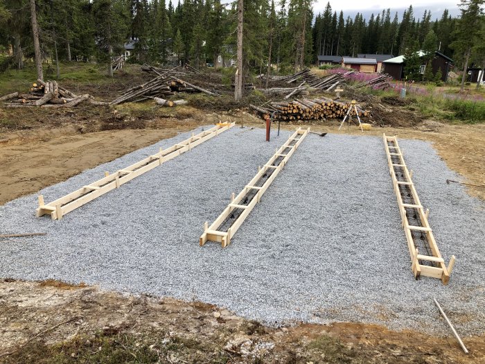 Formsatt och armerad grund för gjutning med grus och träramar på en byggplats i skogsmiljö.