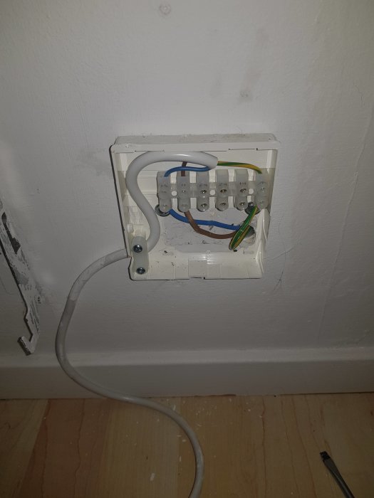 Kopplingsdosa för elektriska element med synliga kablar och kopplingsklämmor mot vit vägg.