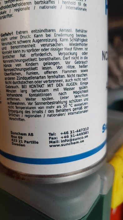 Närbild på etiketten av en sprejburk med varningsinformation och tillverkarens kontaktuppgifter.
