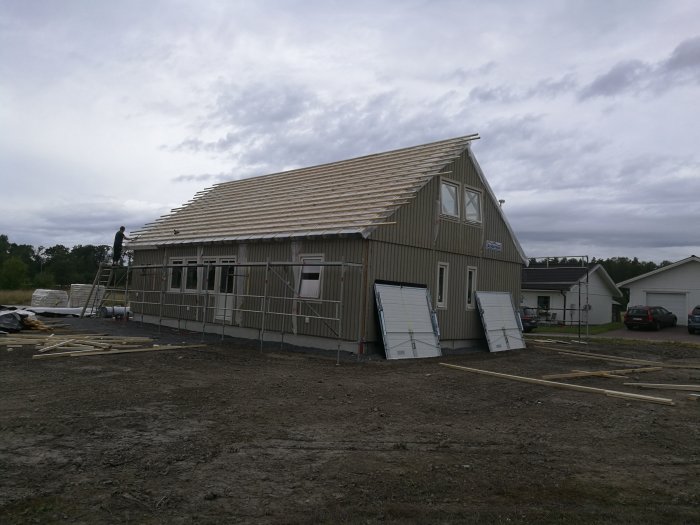 Ett halvfärdigt trähus under konstruktion med takstolar och delvis monterad ytterpanel.