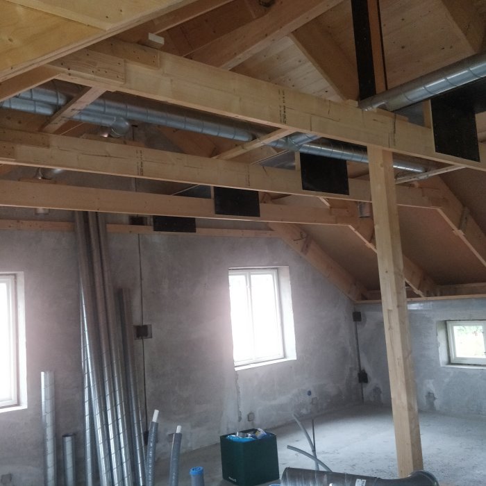 Renoverat vindsutrymme med synliga träbjälkar, ventilationssystem och oavslutade väggar.