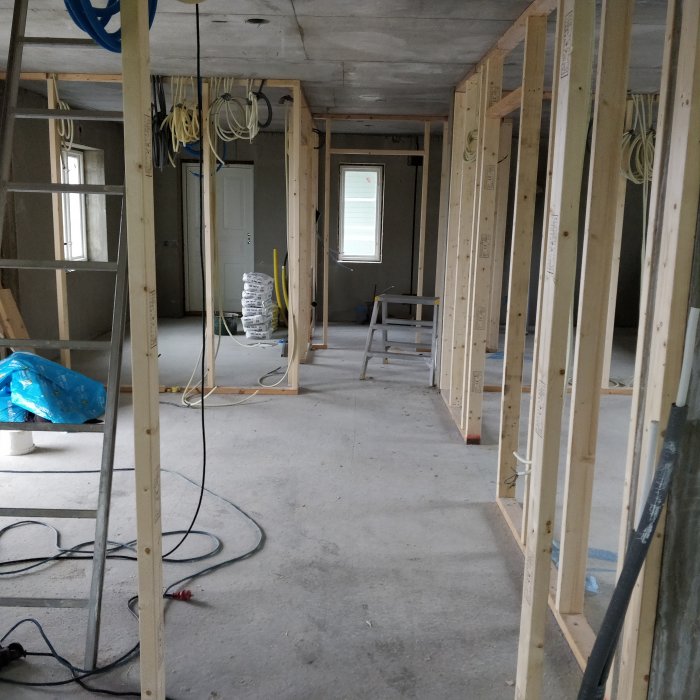 Ouppbyggd interiör i ett hus under renovering med reglade väggar och synliga elinstallationer.