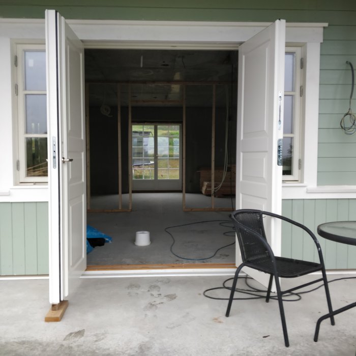 Nybyggd veranda med öppen dörr visar reglade väggar inuti och byggmaterial i bakgrunden.