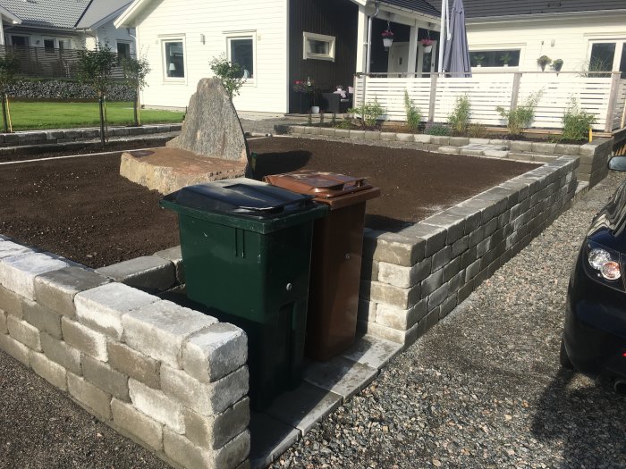 Nybyggd blomlåda med bambuväxter i trädgård efter regn, intill hus och uppfart.