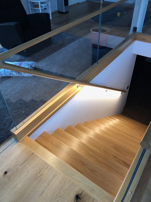 Interiörbild av en nylagt trätrappa med glasräcke och integrerad belysning inomhus.