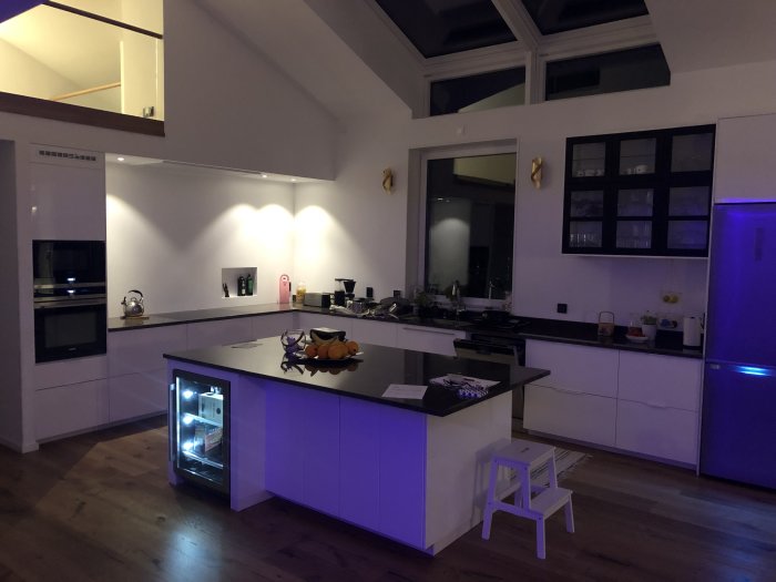 Modernt kök med öppen planlösning och belysning, köksö med inbyggd vinhylla.