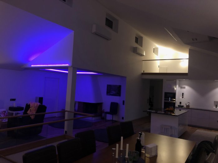 Interiör av modernt vardagsrum med lila LED-belysning, kök i bakgrunden och öppen planlösning.