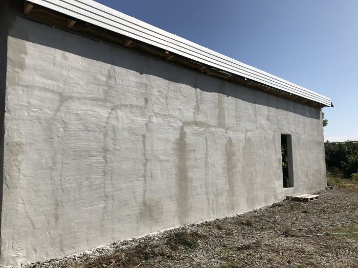 Renoverad husgavel och framsida med nyputsad fasad, synligt taköverhäng och en öppen dörr, under en klar himmel.