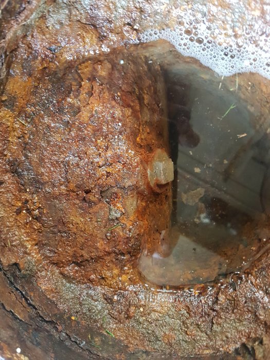 Rostig och igensatt avloppsöppning med synligt vattenlås från 70-talet i garage.