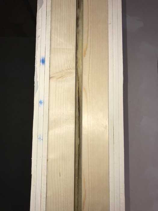 Ljudisolerad väggkonstruktion med tre lager gips, synliga träreglar, isolering och luftspalt.