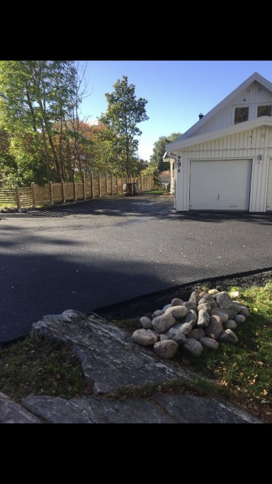 Ny asfalterad uppfart till garage med staket och stenläggning i förgrunden.