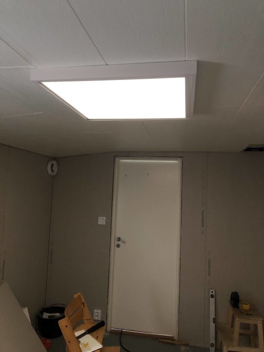 Malmbergs ledpanel Sirius III monterad i taket som lyser upp ett rum under renovering, med synlig dörr och byggmaterial.