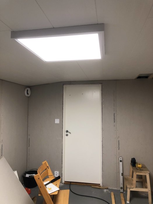 Nyinstallerad Malmbergs ledpanel Sirius III tänd och monterad i taket i ett rum under renovering med oskivade väggar och en stängd dörr.