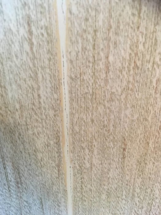 Spricka på en vägg täckt med grov spackel bredvid tapeten med synlig ojämnhet där plattorna möts.