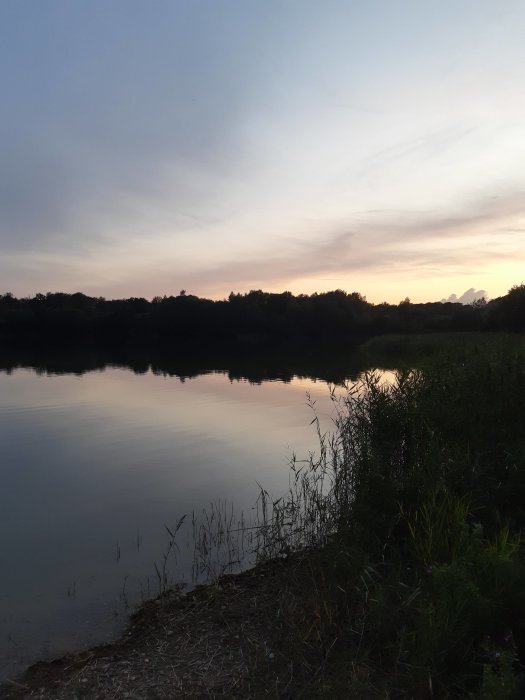 Sjölandskap vid skymning med lugnt vatten och mjuka färger på himlen.