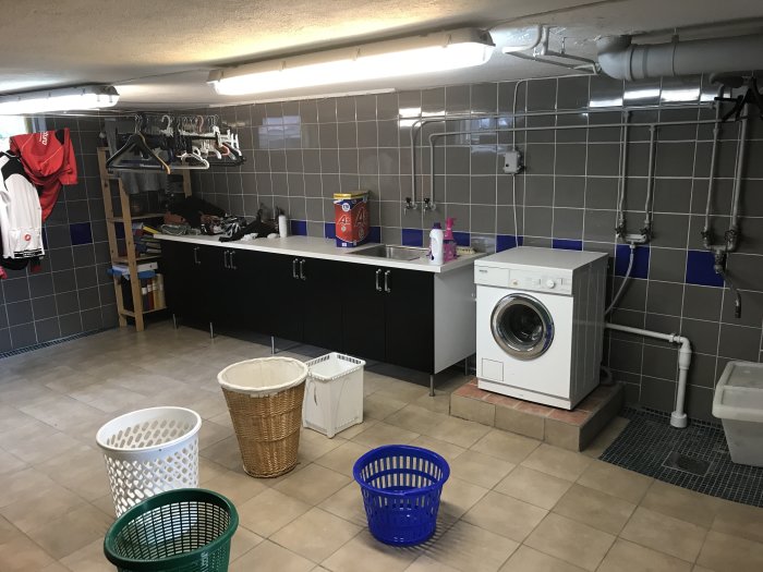 Renoverad tvättstuga med klinkergolv, tvättmaskin, torkställning och svarta skåp.